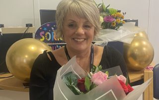 Elaine with gifts and flowers at her retirement celebration with colleagues