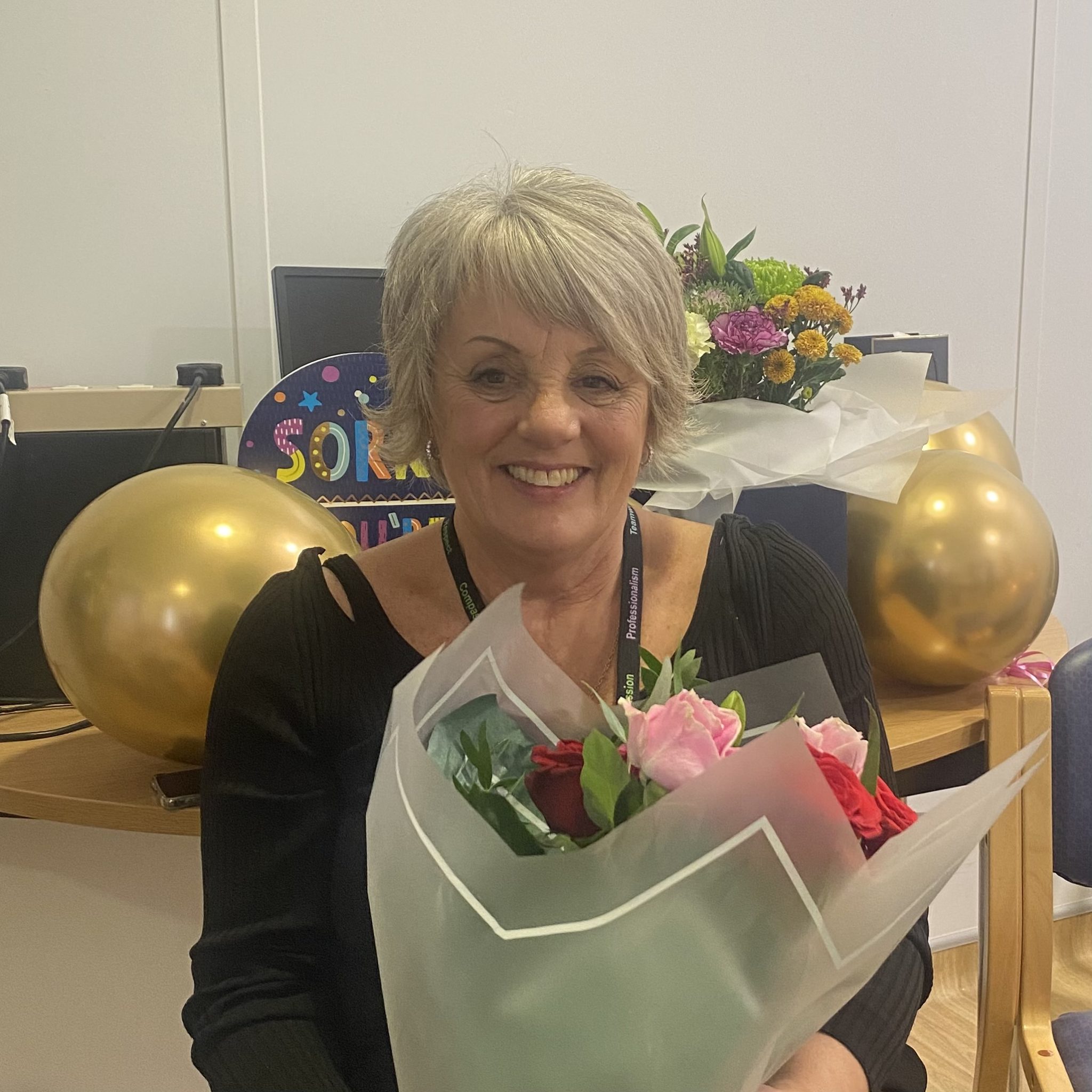 Elaine with gifts and flowers at her retirement celebration with colleagues