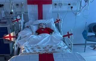Nine-year-old patient Jude Wigley in ward bed, adorned in England flags, celebrates World Cup Game England vs Norway.