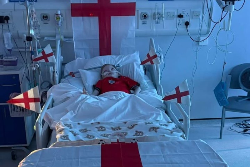 Nine-year-old patient Jude Wigley in ward bed, adorned in England flags, celebrates World Cup Game England vs Norway.