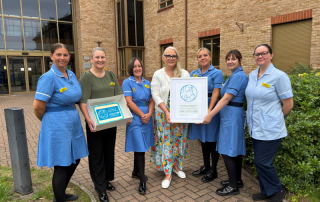Seven members of the 0-19 Health Visiting Service gathered with Baby Friendly Accreditation certificate outside health centre.