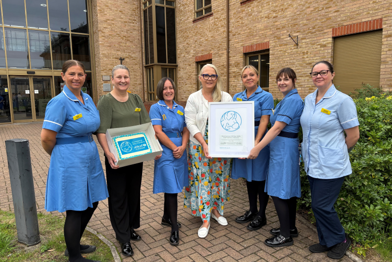 Seven members of the 0-19 Health Visiting Service gathered with Baby Friendly Accreditation certificate outside health centre.